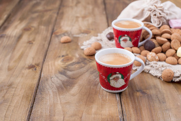 Two cups of aromatic coffee for a good Christmas. Dutch holiday Sinterklaas background, gifts, pepernoten, traditional sweets strooigoed. Flat lay and copy space. Vintage wooden background.