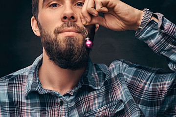 A bearded man wearing a checkered shirt holding a small christmas toy in the background of his face.