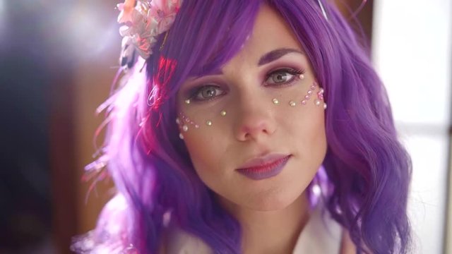 Closeup portrait of a cute girl wearing purple wig and lips, sun light falling on her sparkling face diamods.