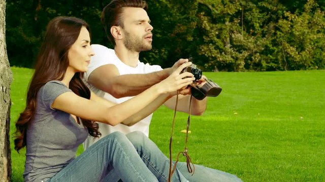 Happy couple taking pictures with an old camera on a green lawn.