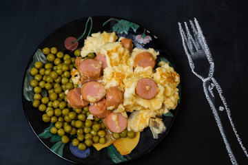 Fried eggs, peas and fried sausages next to a painted fork