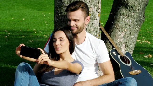 Happy couple taking a picture of themselves with a smartphone on a green lawn.