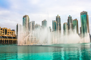 Fototapeta premium Dubai Fountain, największa na świecie fontanna z choreografią na jeziorze Burj Khalifa, o zachodzie słońca gra w rytm wybranej muzyki. W tle wieżowce Starego Miasta w pobliżu centrum handlowego Dubai Mall.