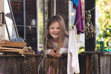 Playful, funny, funny, curious little, young girl on the open veranda of a rural old house in a mess setting posing on camera, smiling and rejoicing in summer