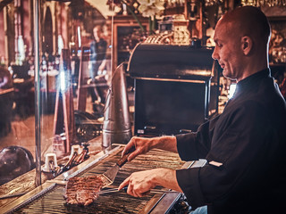 Chef cooking delicious beef steak on a kitchen in a restaurant.