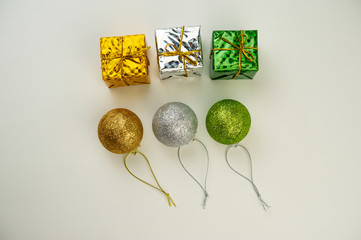 three multi-colored Christmas balls with golden ribbons and boxes with gifts on a light background.