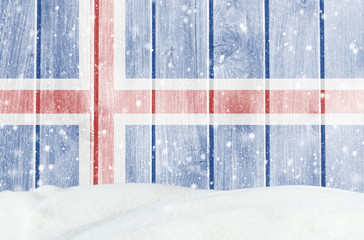 Christmas winter background with wooden wall, falling snow, snowdrift and Icelandic flag