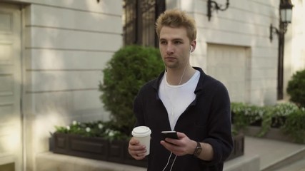 Young man with headphones and coffee walking in the street - Powered by Adobe