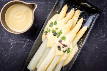 Traditionell gekochter weißer Spargel  mit Sauce Hollandaise und Kräuter als Draufsicht auf einem...