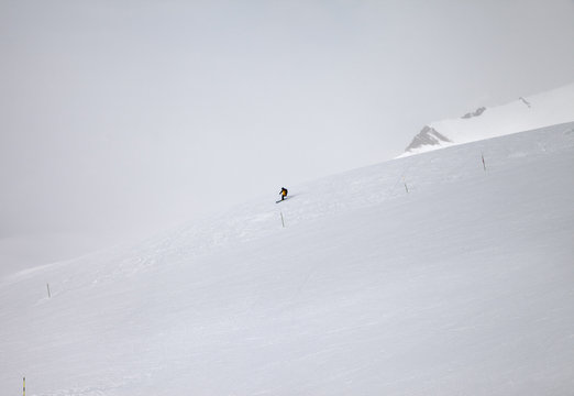 Skier downhill on snowy off-piste ski slope and mountains in fog