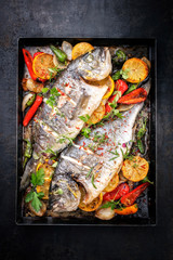 Zwei frisch gegrillte Doraden mit Gemüse und Früchten als Draufsicht auf einem alten Metallblech
