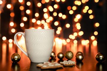 White cup of cocoa or coffee with hot chocolate and marshmallows and gingerbread cookies on the dark brown table and background with golden bokeh. Christmas holiday concept, free space for text