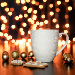 Obraz na płótnie Canvas White cup of cocoa or coffee with hot chocolate and marshmallows and gingerbread cookies on the dark brown table and background with golden bokeh. Christmas holiday concept, free space for text