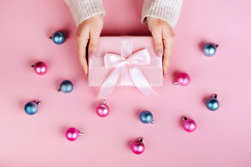 Female hands holding a small gift wrapped with pink ribbon.