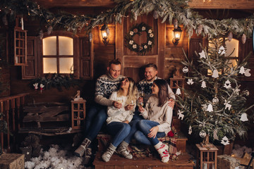 Two married couples are friends. Together celebrate the New Year. Celebrate Christmas. Champagne in the hands of girls and boys. Against the background of a wooden house. Cozy atmosphere