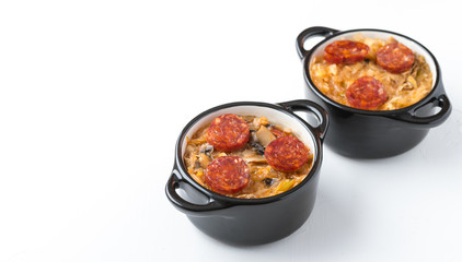 Slovak Christmas national cabbage soup in two small black pots with sausage on the white background.