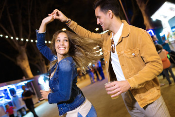 Carefree young couple dancing holding hands in eat market in the street at night.