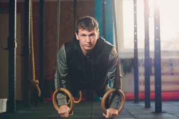 Muscle-up exercise athletic man doing intense workout at the gym on gymnastic rings.