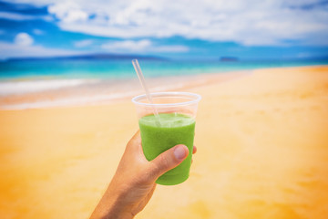 Green smoothie juice detox drink selfie man holding plastic cup on beach summer background. Food picture of healthy nutrition diet in outdoor lifestyle.