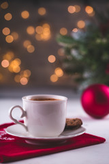 Cup of espresso or americano coffee in white cup in cosy Christmas arrangement, festive decoration with bokeh background, copy space