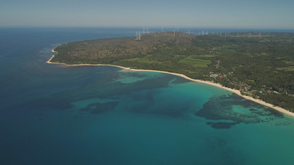 Fototapeta na wymiar Aerial view of beautiful tropical beach Saud with turquoise water in blue lagoon, windmills. Pagudpud, Philippines. Ocean coastline with sandy beach and palm trees. Tropical landscape in Asia.