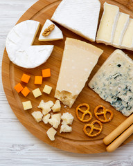Tasting cheese with bread sticks, walnuts and pretzels on bamboo board over white wooden background, top view. Food for wine. From above. Flat lay.