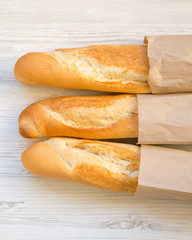 French baguettes in paper bags on white wooden surface, overhead view. Close-up.