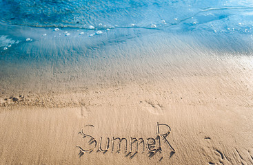 The word summer is written in the sand. The inscription is made by hand. Blue sea wave.