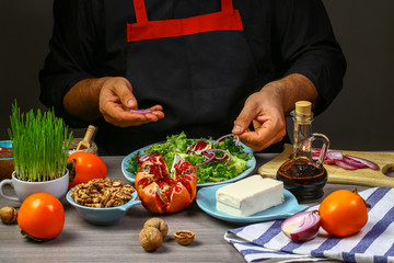 Chef hands cooking salad with persimmon, pomegranate, nuts and feta cheese on dark background. Food concept