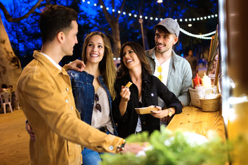 Group of attractive young friends visiting eat market and buying different types of fast food in eat market in the street.
