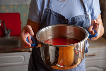 Obraz na płótnie Canvas woman cook prepares tomatoes in a saucepan, rubs through a sieve and prepares tomato juice. Female hands closeup.