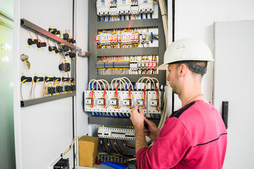 An engineer in a white helmet works in an electrical box. The electrician performs electrical work.