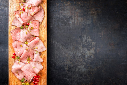 Traditional lunch meat with sliced cold cuts roast beef decorated with red ribes as top view on a cutting board with copy space right