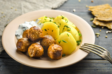 Swedish meatballs with potatoes. Garlic sauce, fresh herbs and cereal tortilla. Dish of national cuisine on a wooden table.