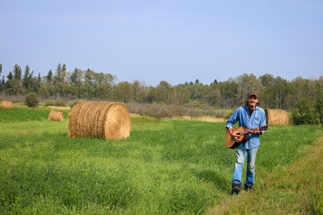 Naklejka na ściany i meble Handsome man playing a and acoustic guitar in the field