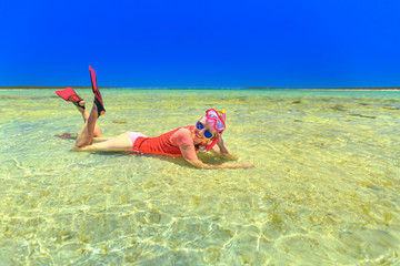 Happy caucasian woman with snorkeling wetsuit, mask and fins pink and peach color, sunbathing lying in the tropical natural pool of Little Lagoon in Shark Bay, Denham, Western Australia. Copy space.