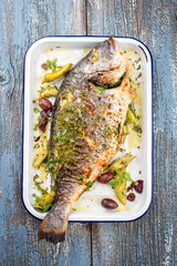 Fresh Greek barbecue gilthead seabream with peperoni and Kalamata olives as top view in a white skillet