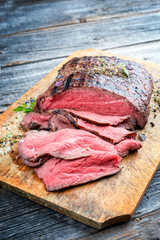 Traditional barbecue dry aged sliced roast beef steak with herbs as closeup on an old cutting board with copy space - obrazy, fototapety, plakaty