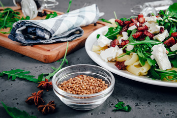 Dish with Arugula on a white plate. Green, fresh arugula on a plate, with white cheese and pasta on a stone countertop. The concept of preparing a fresh and healthy salad. Caring for health.