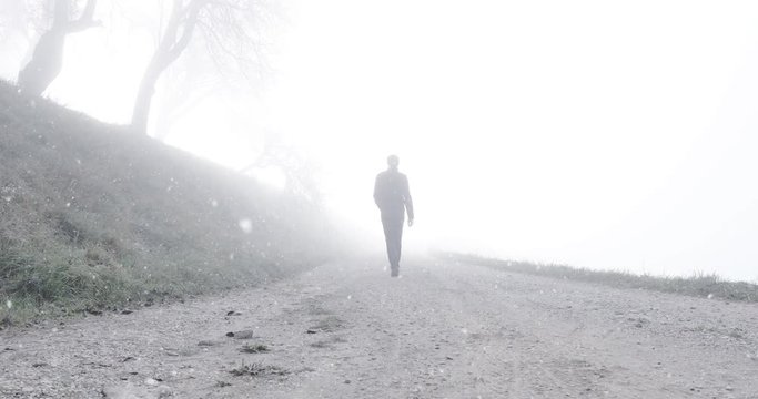 Man walks alone on foggy winter season countryside road durnig snowfall. 