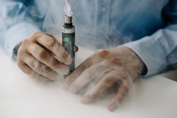 The man uses an e-cigarette, a lot of smoke around. The concept of using e-cigarette, vaping. Addiction to nicotine, topping up liquid. Problems with addiction.