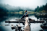Side view of a woman sitting on driftwood in forest