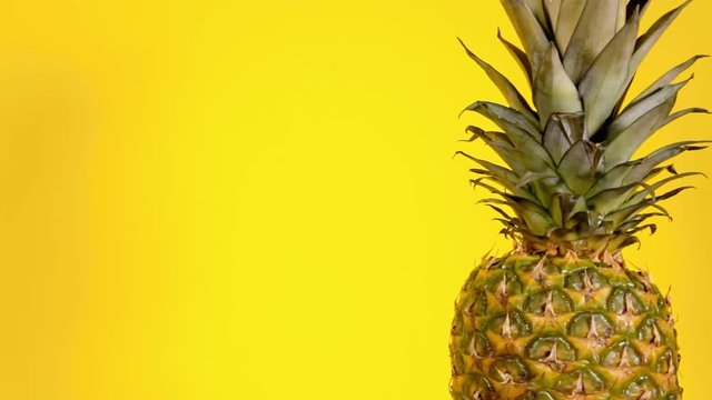 A ripe whole ananas (exotic fruit) on a slowly rotating surface. Yellow background, side close-up shot.