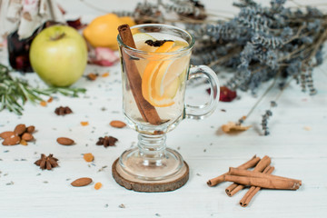 mulled wine in glass cup on white table with cinnamon, fruits and flowers on background