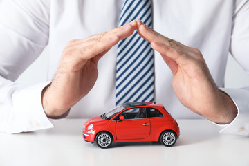 Male insurance agent covering toy car at table, closeup