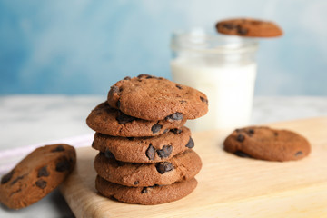 Wooden board with stack of tasty chocolate chip cookies on table