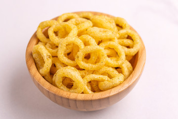 Puff corn rings in wooden bowl on light background