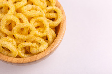 Puff corn rings in wooden bowl on light background