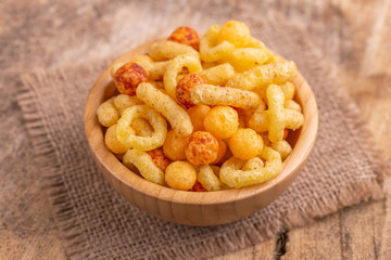 Mixed puff corn snacks in wooden bowl on burlap napkin