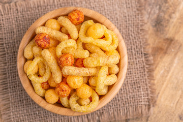 Mixed puff corn snacks in wooden bowl on burlap napkin